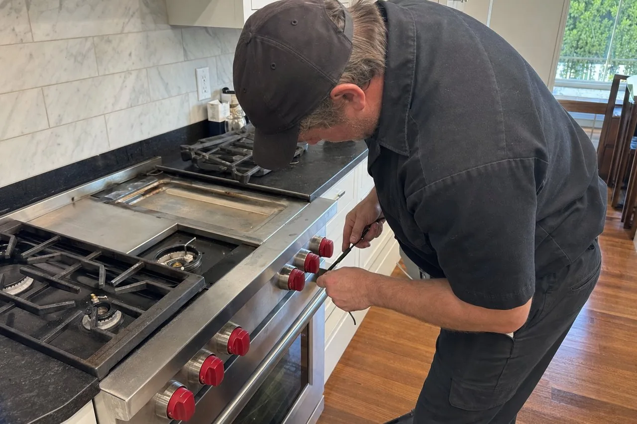 Technician servicing a stainless Wolf range in a Sands Point kitchen